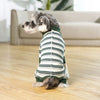 A grey dog wearing a striped green and white jumpsuit lies on a wooden floor.