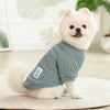 A fluffy white dog wearing a gray knitted winter sweater sitting on a light surface.