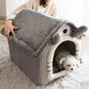 A gray removable dog house pet bed with a soft interior, resting on a fluffy white rug.