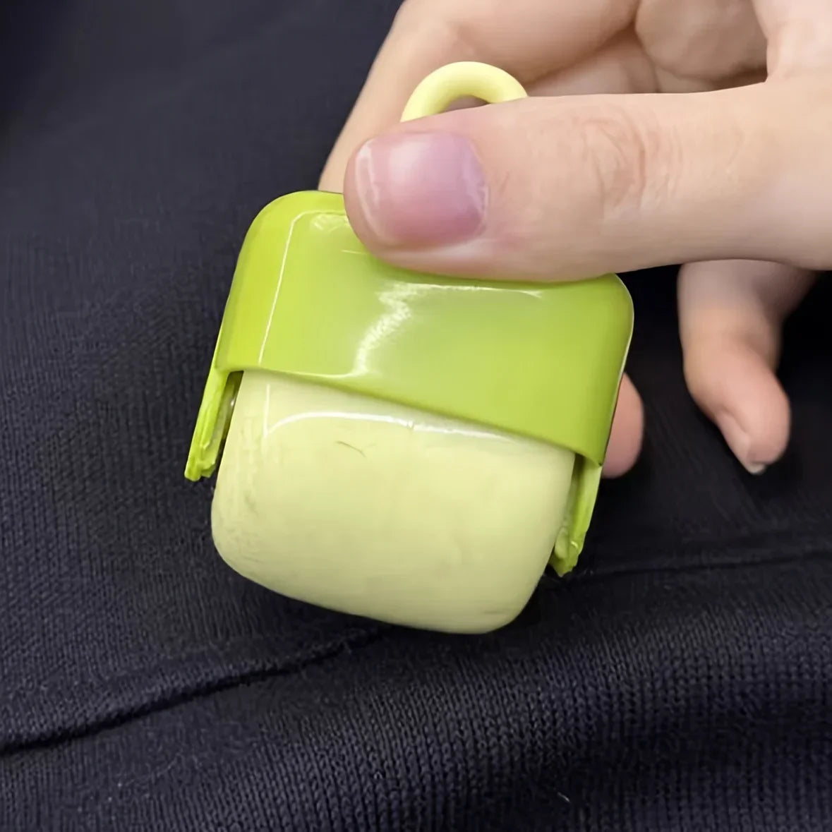 A hand is holding a lime green portable lint roller for pet hair removal against a dark background.