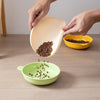 A hand is pouring coffee beans from a yellow bowl into a light orange silicone feeding mat for pets.