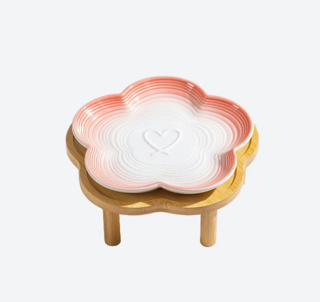 Un bol pour animaux en céramique avec un émail dégradé rose et blanc repose sur un support en bois naturel.