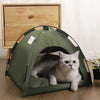 A fluffy gray cat is relaxing inside a green fabric pet tent bed on a wooden surface.