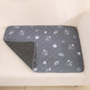 A gray reusable washable pet training mat with a repeating pattern of white paw prints and pet silhouettes is placed on a lig
