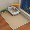 A white cat litter mat is placed on a wooden floor next to a window, with a small potted plant nearby.