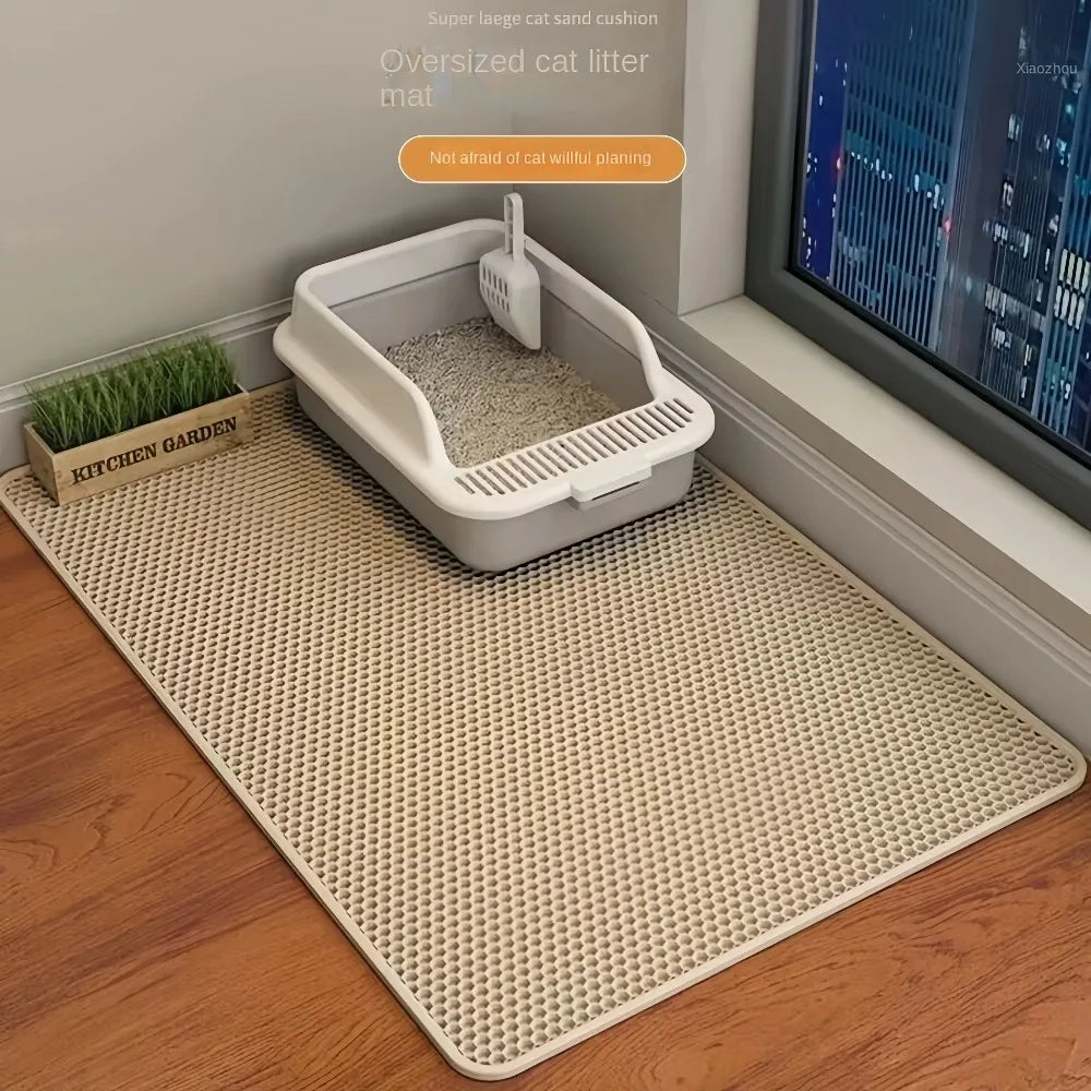 A white cat litter mat is placed on a wooden floor next to a window, with a small potted plant nearby.