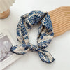 Écharpe en coton à motif floral bleu et blanc nouée, posée sur un objet en bois clair.