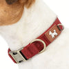 A close-up of a maroon dog collar with a tan silhouette tag on a white dog's neck.