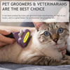 A tabby cat is being groomed by a person using a purple pet deshedding brush.