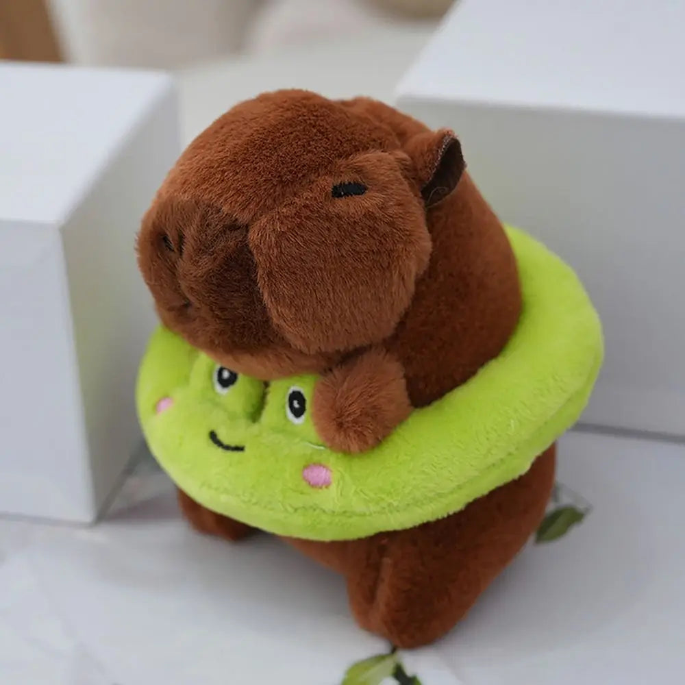 A brown capybara plush doll wearing a lime green hoodie and wings, sitting on a white surface.