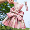 Pink plaid dog dress with bow and matching harness being held by a person.