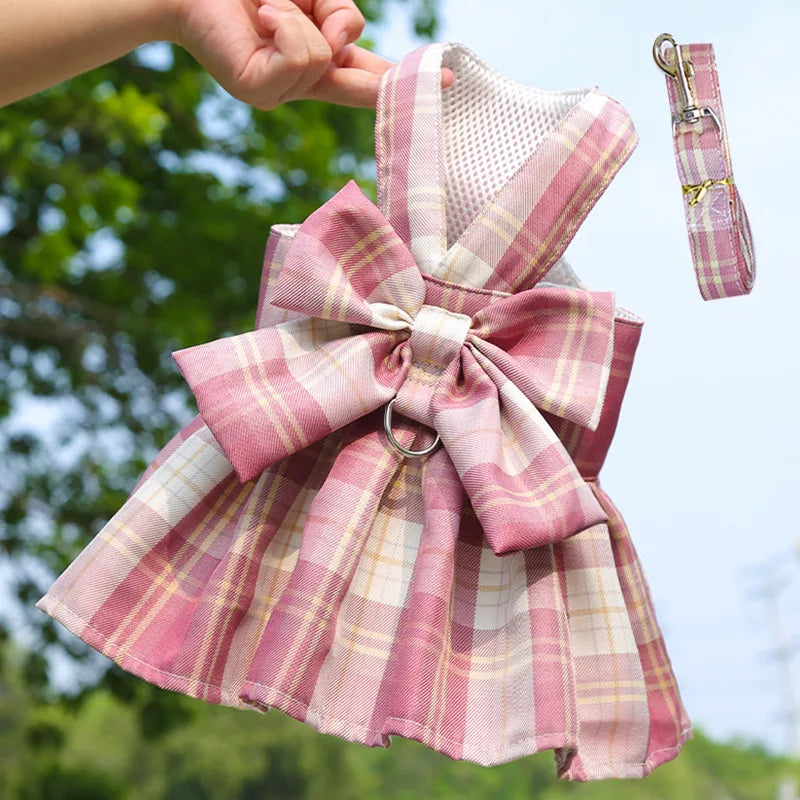 Pink plaid dog dress with bow and matching harness being held by a person.