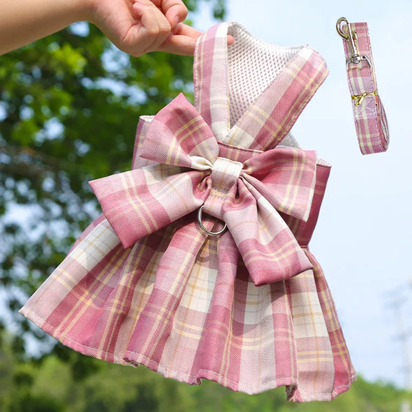 Pink plaid dog dress with bow and matching harness being held by a person.