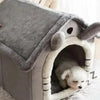 A gray pet house with a round entrance and soft lining, positioned on a white fluffy surface.