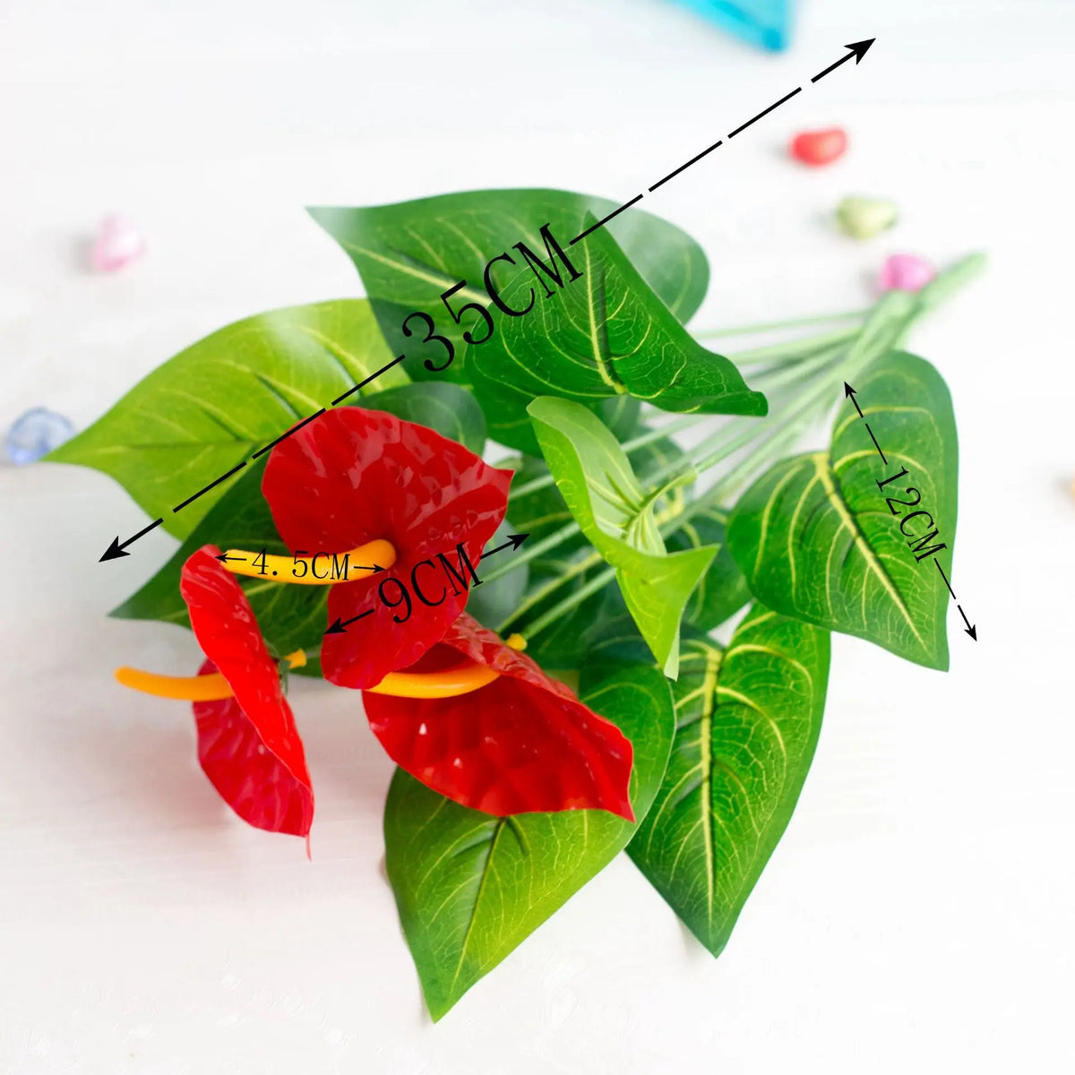 Künstliche Anthurium-Pflanze mit großen grünen Blättern und roten Kelchblättern, die verschiedene Maße zeigt.