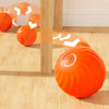 Oranger automatischer Springball für Haustiere auf einem Holzfußboden neben einem vertikalen Holzpfahl.