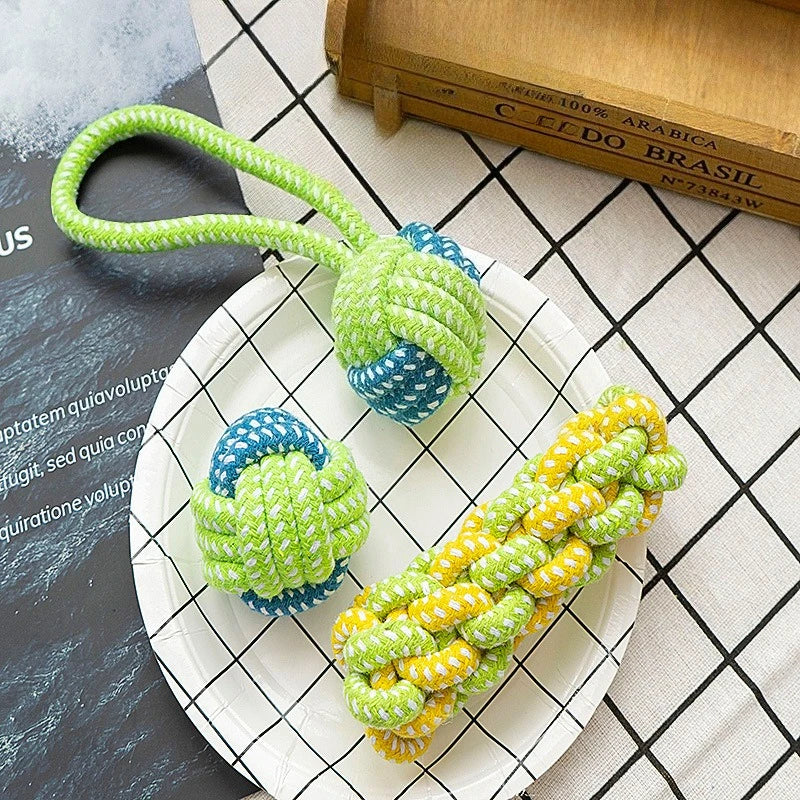 A bright green rope ball dog toy is displayed on a white plate next to a wooden box.
