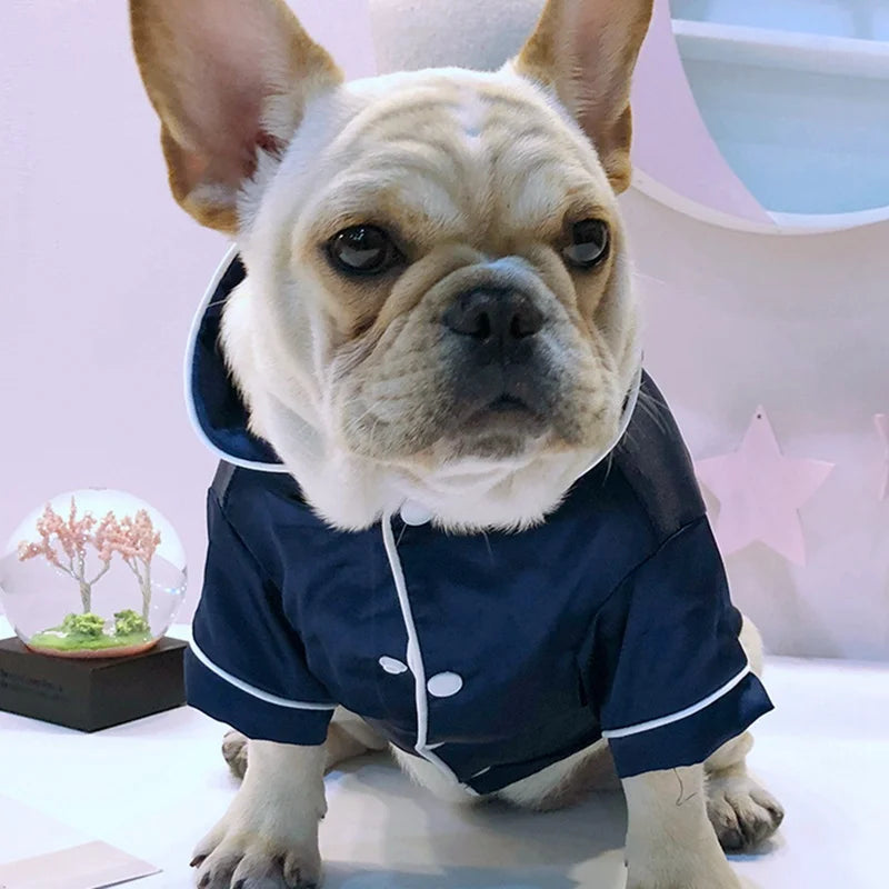 A fawn-colored French Bulldog wearing a dark blue silk pet pajama top.