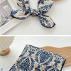 Foulard en coton bleu et crème à motif noué en nœud, exposé à côté d'un objet en bois.
