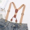 Tan suspenders with brown leather accents worn over a denim jean pocket.