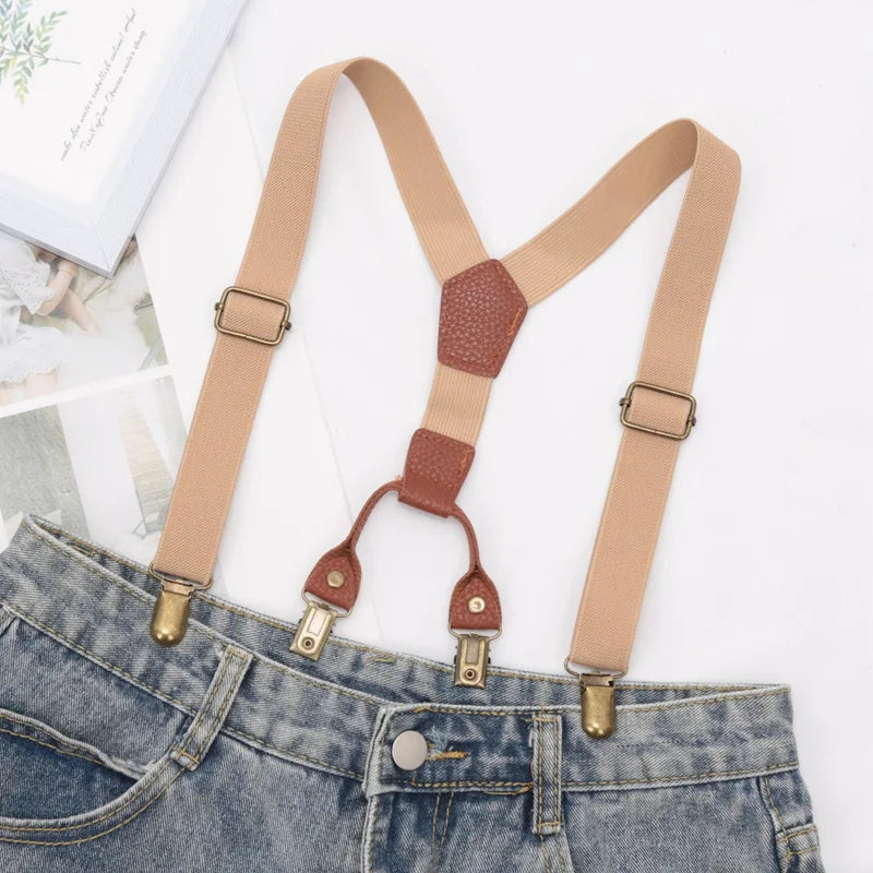 Tan suspenders with brown leather accents worn over a denim jean pocket.