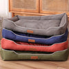 A stack of waterproof orthopedic dog beds in various colors including gray, blue, and orange resting on a wooden surface.