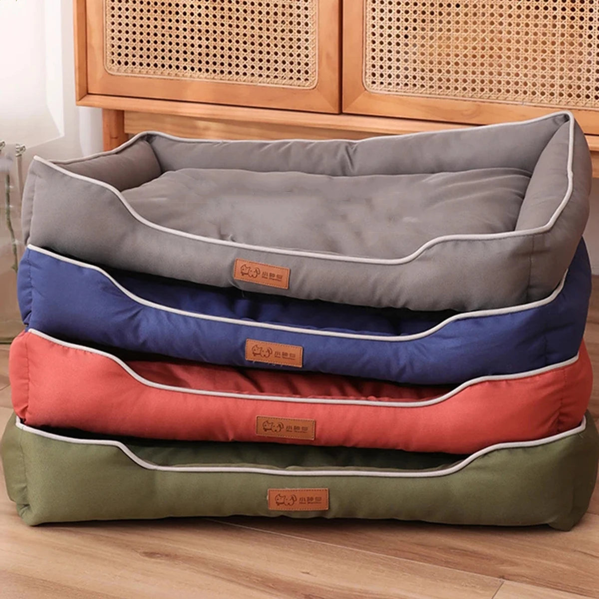 A stack of waterproof orthopedic dog beds in various colors including gray, blue, and orange resting on a wooden surface.