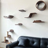 Wall-mounted cat tree with scratching stairs and hammock mounted on a white wall above a black leather sofa.