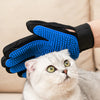 A white cat looks up at a hand wearing blue silicone pet grooming gloves.