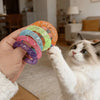 A cat is interacting with a hand holding a set of colorful mesh donut chew toys.