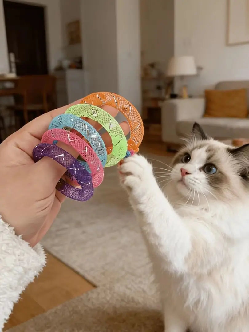 A cat is interacting with a hand holding a set of colorful mesh donut chew toys.