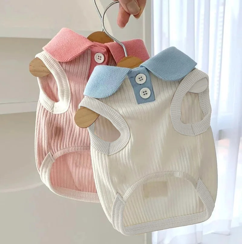 A light beige dog shirt with a blue lapel collar and white buttons is displayed on a wooden hanger.