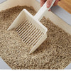 A hand is using a white extra-large cat litter scoop with a hanging hook to move dry cat litter in a container.