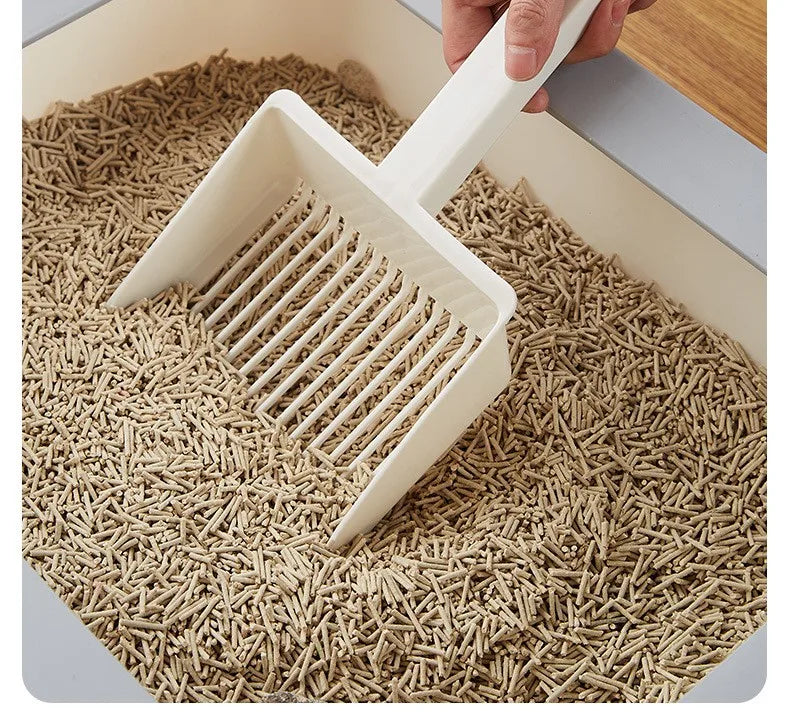 A hand is using a white extra-large cat litter scoop with a hanging hook to move dry cat litter in a container.