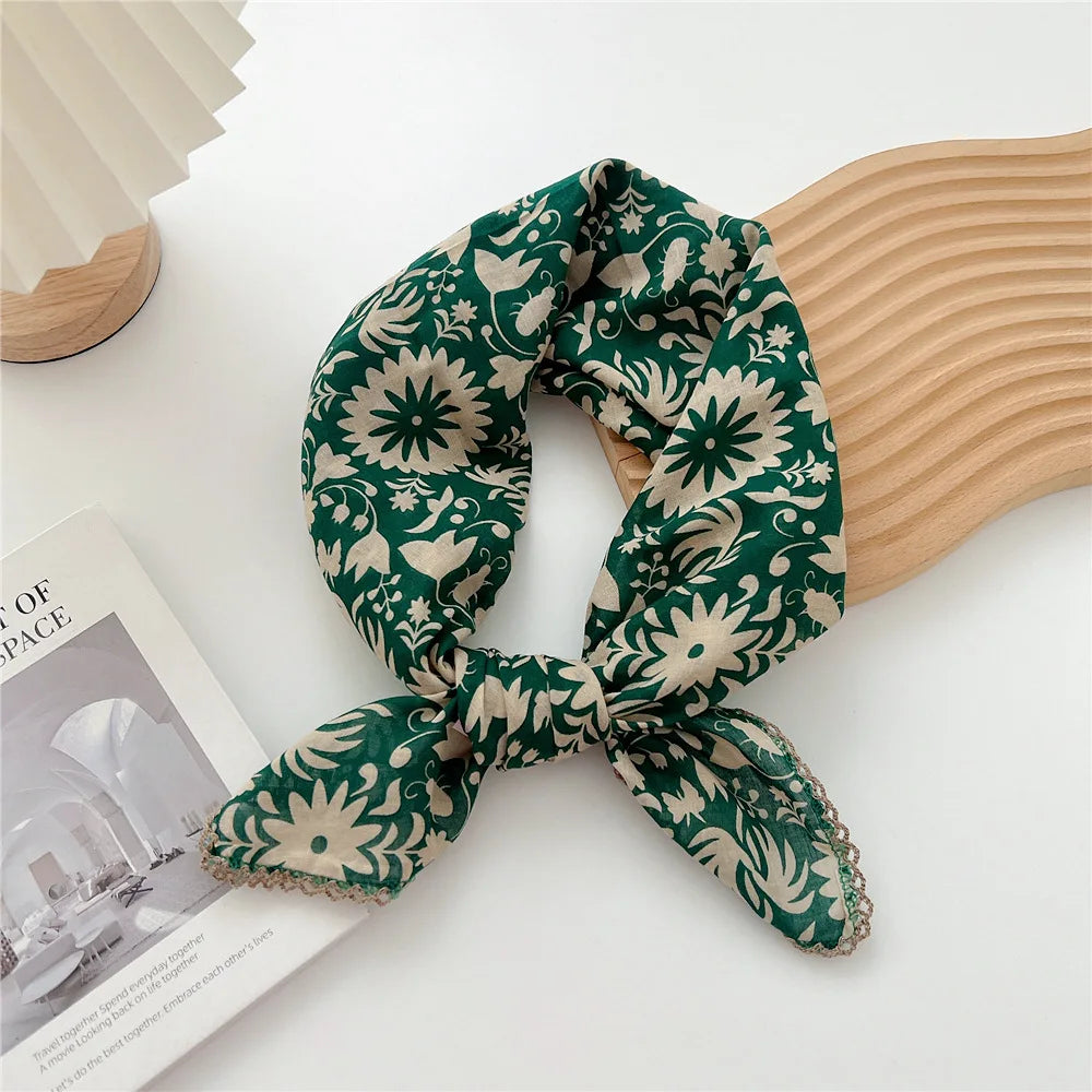 Écharpe en coton à motifs vert et crème nouée en nœud, posée sur un objet en bois clair.