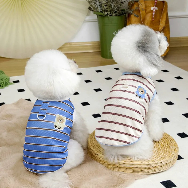 A fluffy white dog wearing a blue striped cooling vest sits on a light rug.