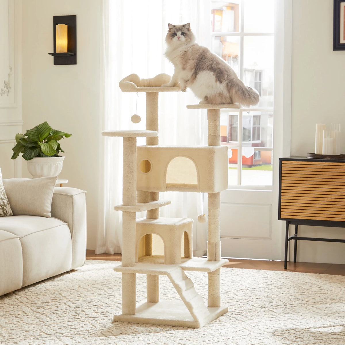 A light beige cat tree tower with multiple tiers and sisal scratching posts stands next to a window.