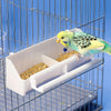 Un perroquet budgerigar jaune et vert nourri d'un distributeur automatique de nourriture blanc dans une cage en fil de fer.