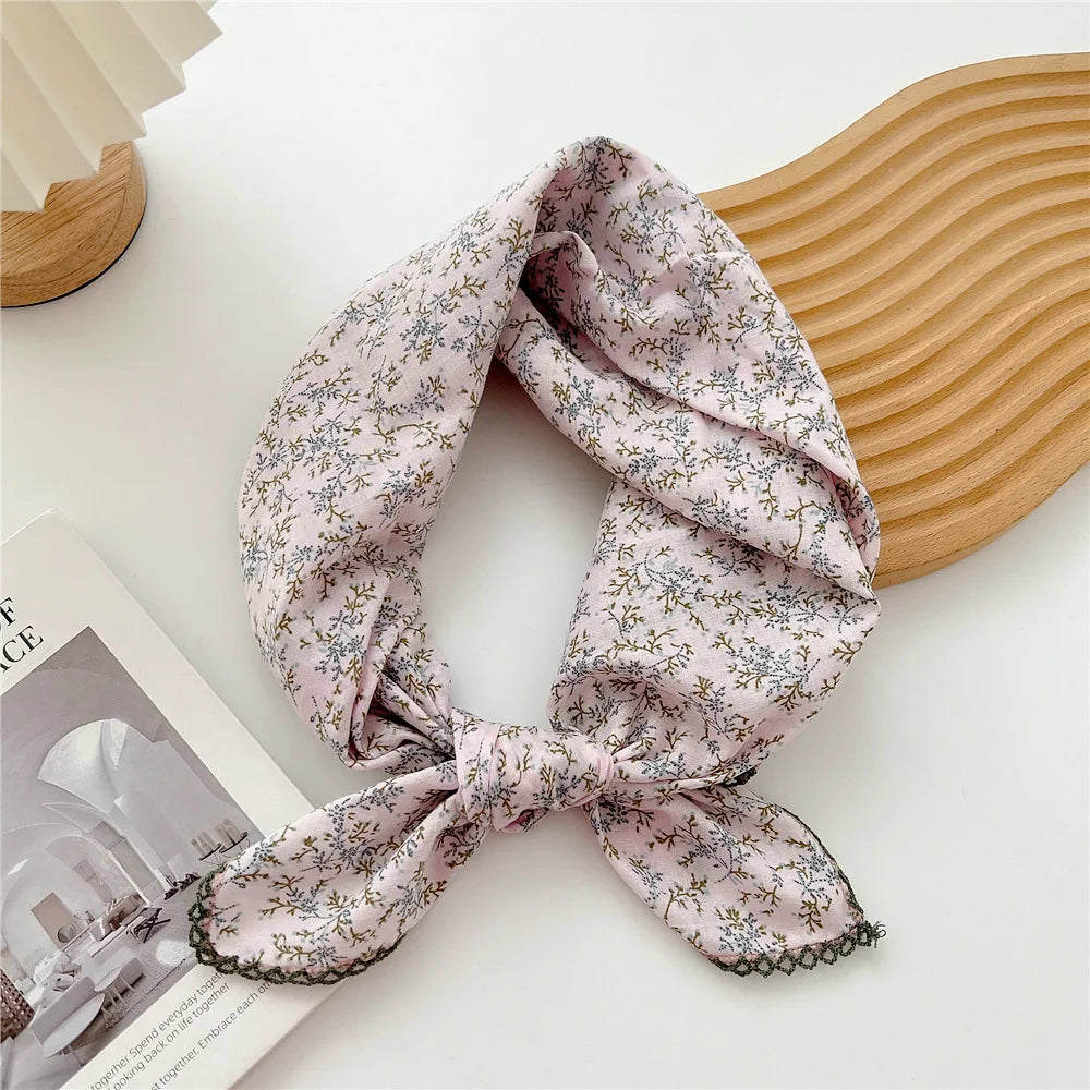 Écharpe en coton florale rose pâle nouée en nœud posée sur une spatule en bois.