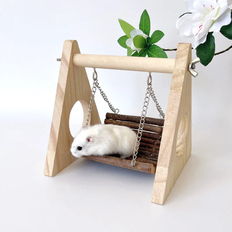 Juguete de columpio para hámster de madera con un hámster blanco pequeño colgando de una cadena.