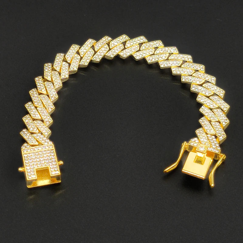 Pulsera de cadena cubana dorada con piedras de imitación claras, exhibida contra un fondo oscuro.