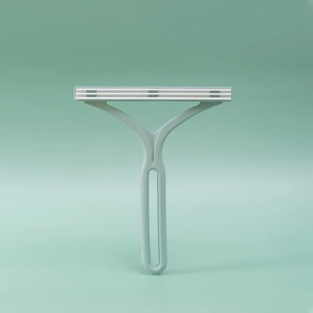 A white manual lint remover brush with a flat bar and a curved handle against a light green background.