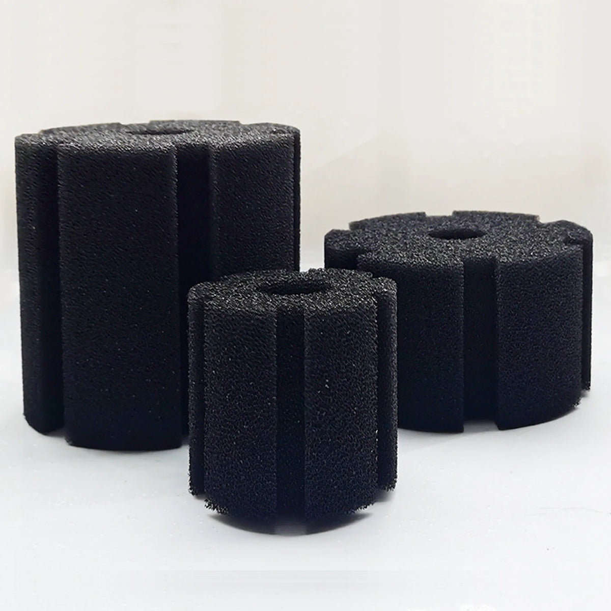 Three black biological aquarium sponge filters standing upright on a white surface.