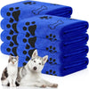 Ein Stapel blauer Mikrofaser-Tierbadtücher mit schwarzen Pfotenabdruck-Designs neben einem weißen Hund.