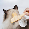 A hand is using a stainless steel pet hair remover brush on the fur of a cat.
