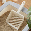 A white extra-large cat litter scoop with a hanging hook is shown resting on a bed of light brown cat litter inside a gray pl
