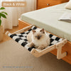A solid wood hanging cat hammock with a black and white patterned fabric is shown on a light-colored carpet.