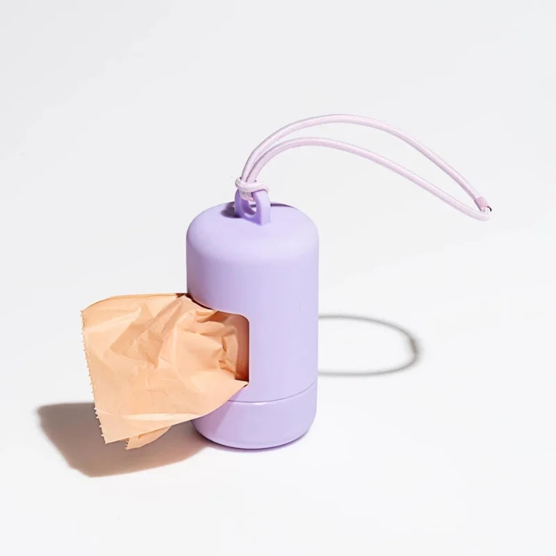 A purple portable dog poop bag dispenser with a pink strap and an open cardboard bag.