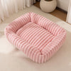 Un lit pour animaux en peluche rose à côtes pour chiens et chats, posé sur une moquette blanche.