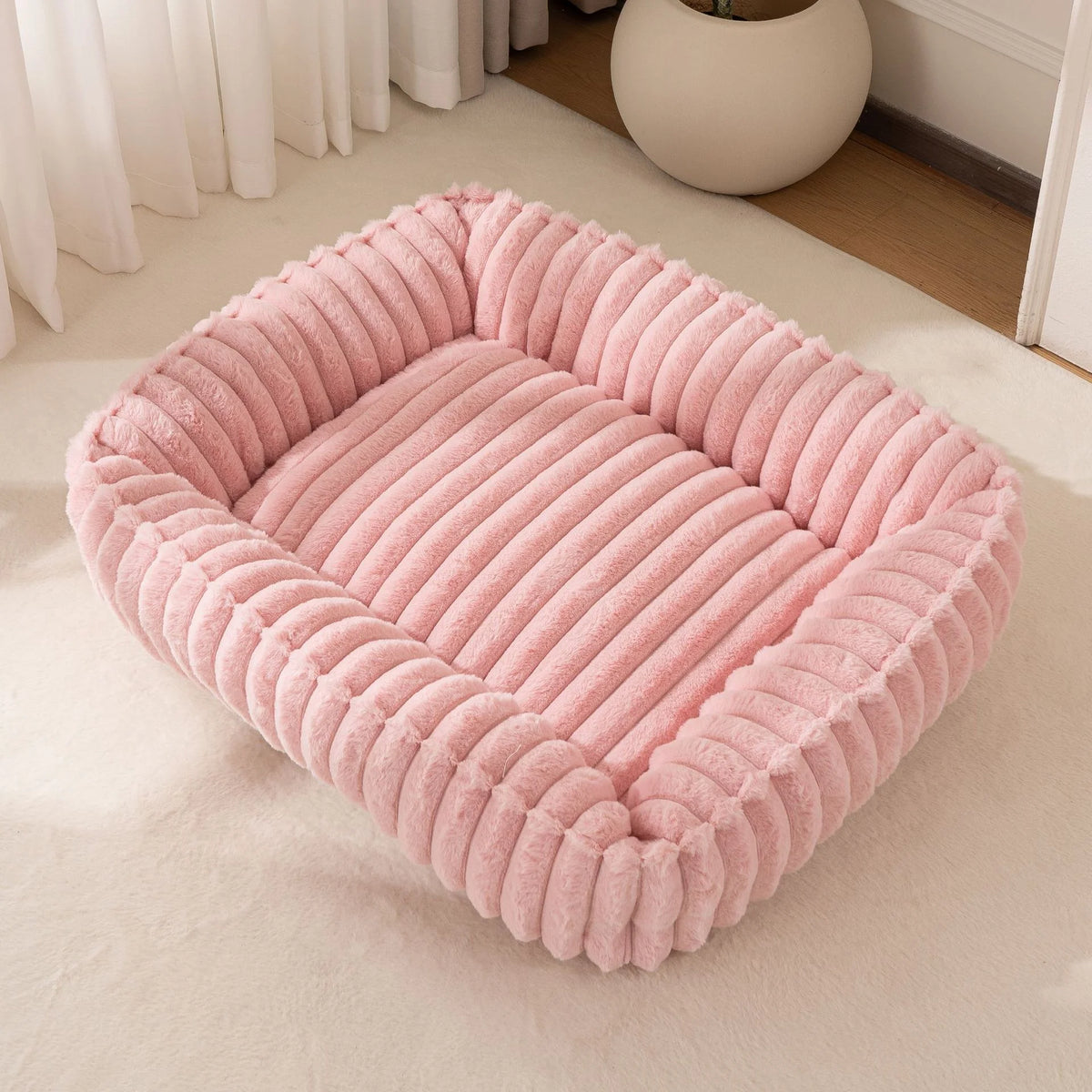 Un lit pour animaux en peluche rose à côtes pour chiens et chats, posé sur une moquette blanche.